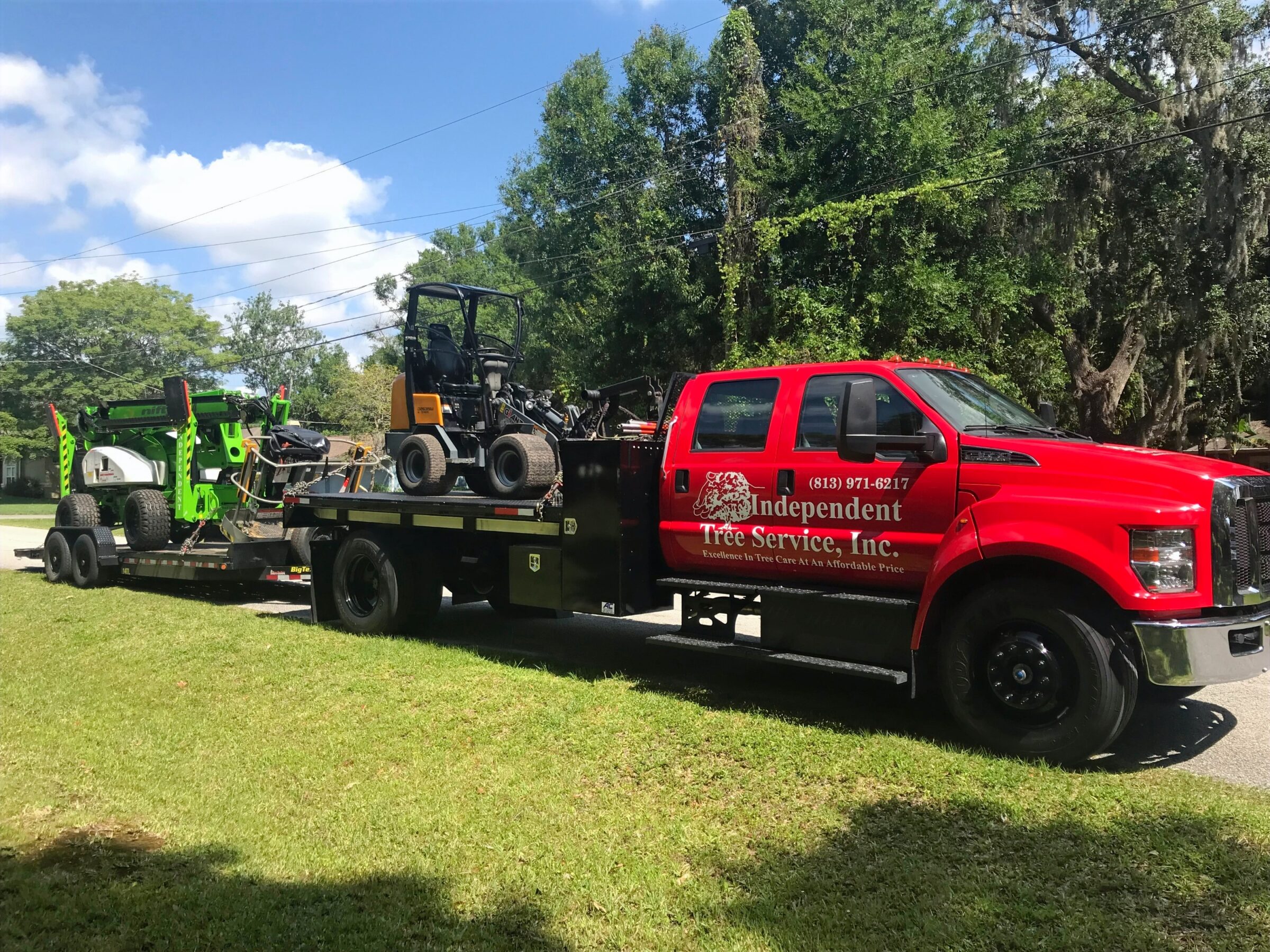 A red truck from Independent Tree Service, Inc. is towing green tree service equipment on a trailer.